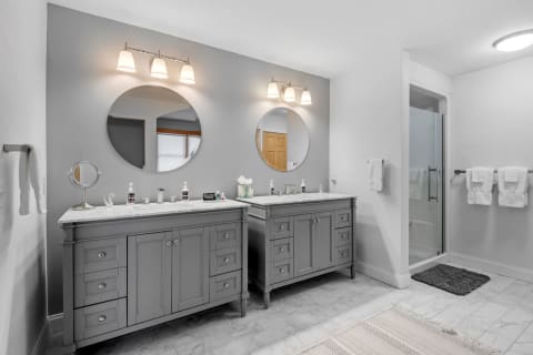 Modern bathroom with gray vanities, mirrors, and a glass shower.