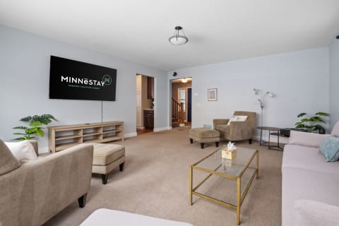 A cozy living room with light blue walls, two armchairs, a sofa, and a TV displaying MINNESTAY logo.