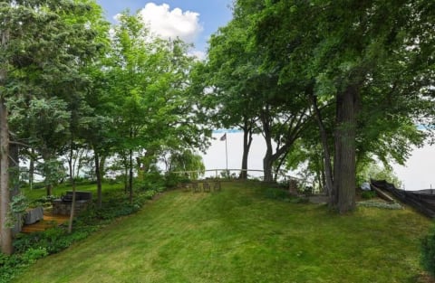 A scenic view of a green lawn leading to a lake, surrounded by trees.