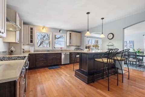 A modern kitchen featuring dark wood cabinetry, stainless steel appliances, and a bright view through large windows.