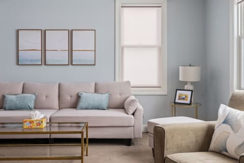 A living room with a beige sectional sofa, light blue walls, and decorative art.