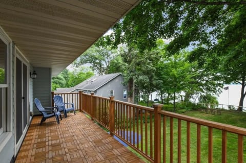 A balcony with two blue chairs overlooking a green yard and water.