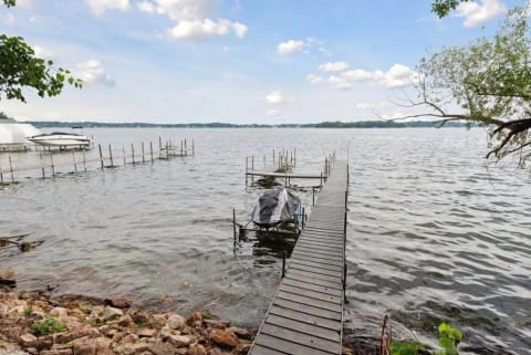 A wooden dock extending into calm lake waters with a covered boat and greenery nearby.