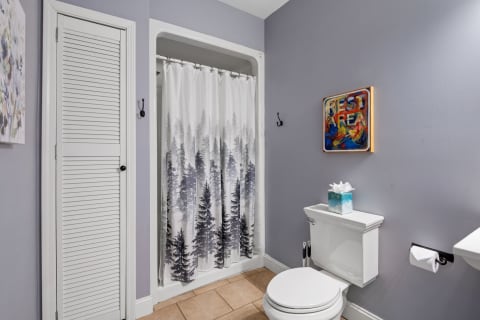 A bathroom with purple walls, a nature-inspired shower curtain, and colorful decor items.