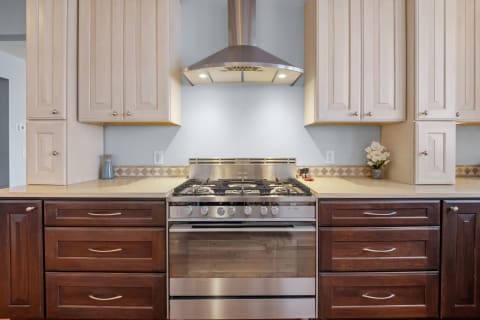 A modern kitchen with a stainless steel gas range, dark wood drawers, and light-colored cabinets.