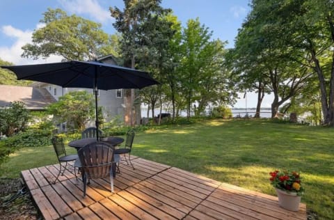 Backyard with a wooden deck, black umbrella, and view of a lake.