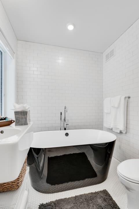 Modern bathroom with a black and white freestanding bathtub and subway tiled walls.