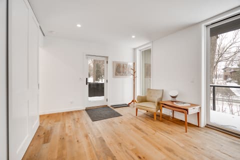 Bright entryway with wooden floors, a chair, and natural light from large windows.