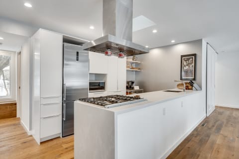 Modern kitchen with white cabinets, stainless steel appliances, and wooden flooring.