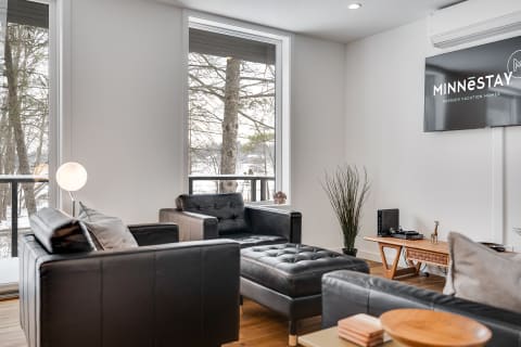 Stylish living room with black leather furniture and large windows overlooking trees.