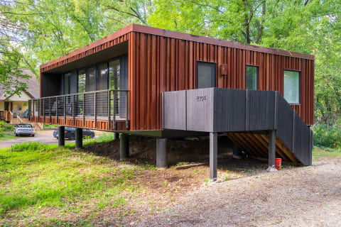 A modern elevated home with a rust-colored exterior among green trees.