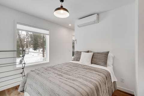 A modern bedroom featuring a bed with a gray quilt and a view of snow-covered trees outside.