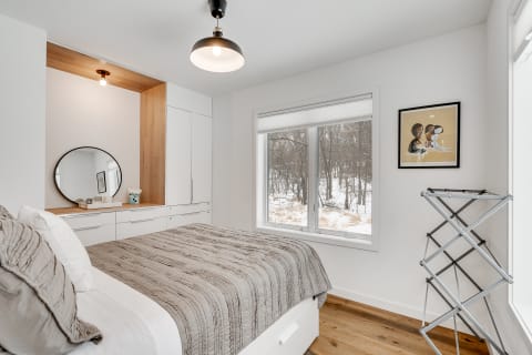 A modern bedroom with a gray quilted bed, wooden accents, and a snowy landscape outside the window.