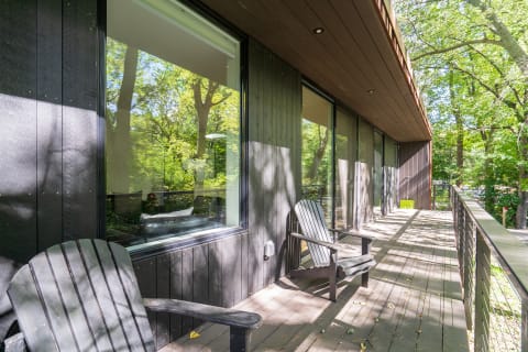Modern wooden terrace with black chairs amidst a green forest background.