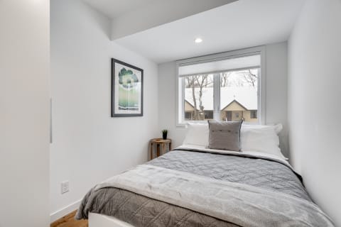 Cozy bedroom featuring a grey blanket and a view of snow-covered rooftops through a window.