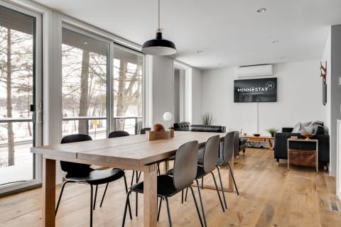 Modern dining area featuring a wooden table and black chairs with large glass doors and snowy scenery outside.