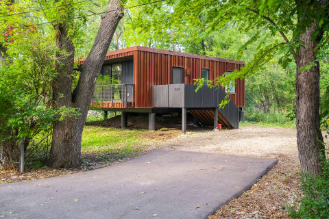 A contemporary house with wood paneling surrounded by greenery, featuring a deck and elevated structure.