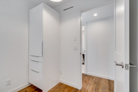 Interior view of a minimalist hallway with a tall white cabinet and a doorway leading to another room.