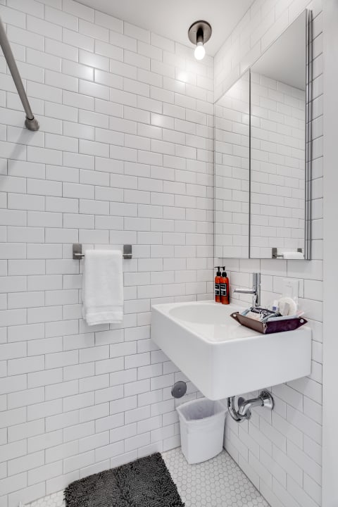 A contemporary bathroom with a white subway tile wall, a wall-mounted sink, and neatly arranged toiletries.