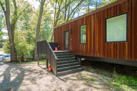 A modern house with a corrugated exterior, stepping from a gravel path surrounded by trees.