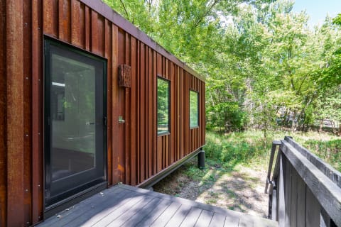 A contemporary cabin with a rust-colored metal exterior and large windows, surrounded by trees.