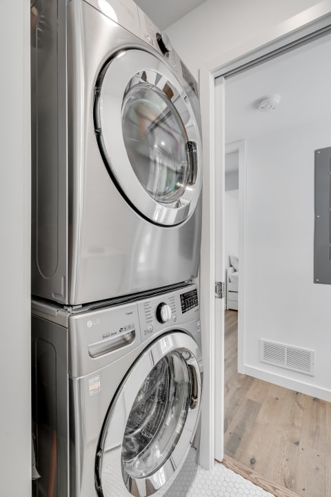 A stainless steel stacked washer and dryer in a bright laundry room.