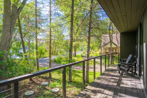 A balcony overlooking trees and a winding road leading to a house.