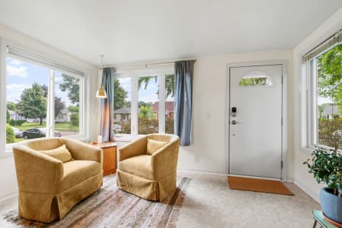 A sunlit living room with two armchairs and large windows, showcasing a suburban view.