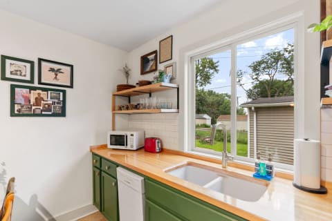 Cozy kitchen with natural light, green cabinets, and open shelving.