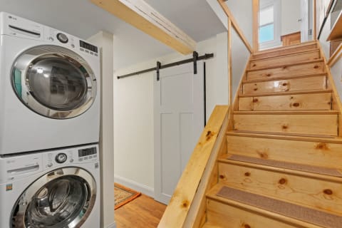 Laundry appliances beside a wooden staircase with a sliding barn door.