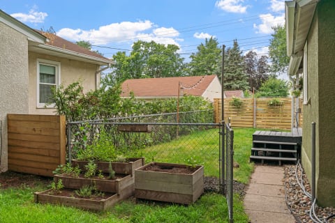 Backyard scene featuring garden beds, a wooden deck, and a clear sky.