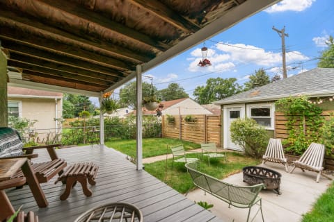Backyard patio with wooden structure, green chairs, and a fire pit.