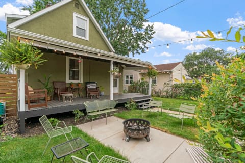 Backyard view with a green house, porch, seating area, and fire pit.