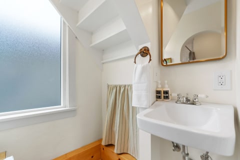 A compact bathroom with a wall-mounted sink, white towel, and frosted glass window.