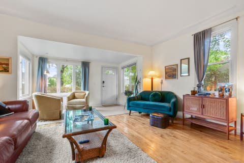 Cozy living room featuring a leather sofa, beige armchairs, and a teal couch with large windows.