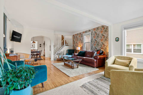 A spacious living room featuring a teal sofa, leather couch, and floral wallpaper.