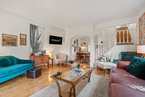 A living room with a turquoise couch, wooden furniture, and a visible dining area in the background.