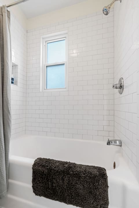 Clean modern bathroom with white subway tiles and a plush towel draped on the bathtub.