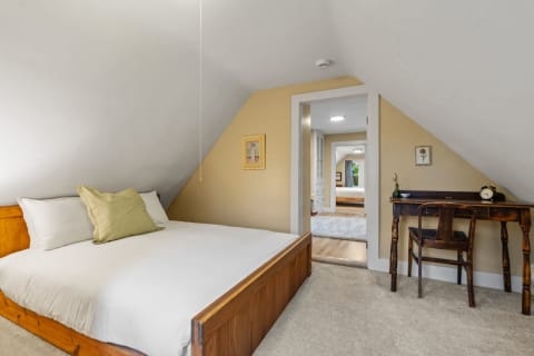 A cozy attic bedroom featuring a wooden bed, soft bedding, and a small desk.