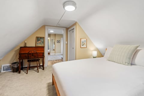 Attic bedroom featuring a bed, vintage desk, and decorative artwork.
