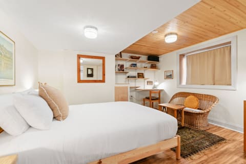 A modern cozy bedroom with a wooden ceiling, white bed, and a wicker chair.