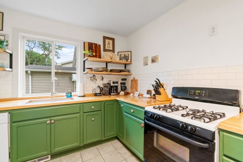 A cozy kitchen with green cabinets and wooden countertops, showcasing various kitchen appliances and decorative items.