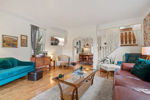 An inviting living room showcasing a teal sofa, wooden elements, and a dining area in the background.