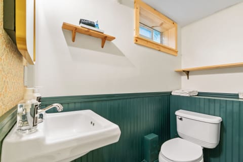 Small bathroom with white sink, green wainscoting, and wooden shelves.