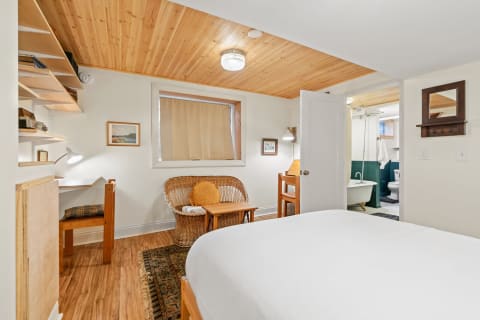 Cozy bedroom with a wooden ceiling, a large bed, and a small workspace.