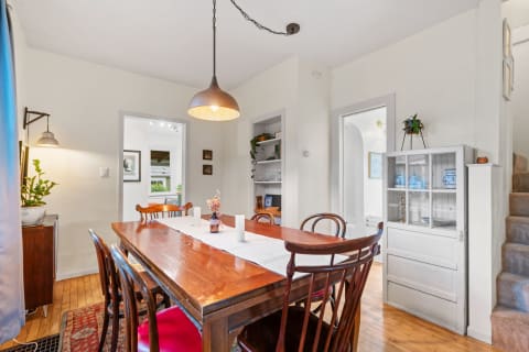A bright dining room featuring a long wooden table with a table runner and chairs, illuminated by a pendant light.