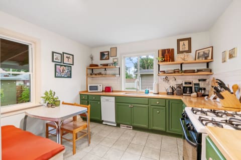 A cozy kitchen with green cabinets, wooden counters, and a small dining area.