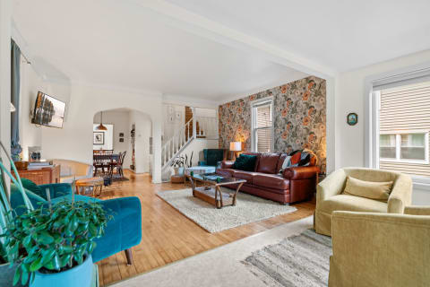 Spacious living room with teal and leather furniture, floral wallpaper, and a dining area in the background.