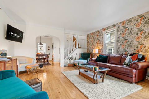 Cozy living room with floral wallpaper, brown leather sofa, and dining area visible in the background.