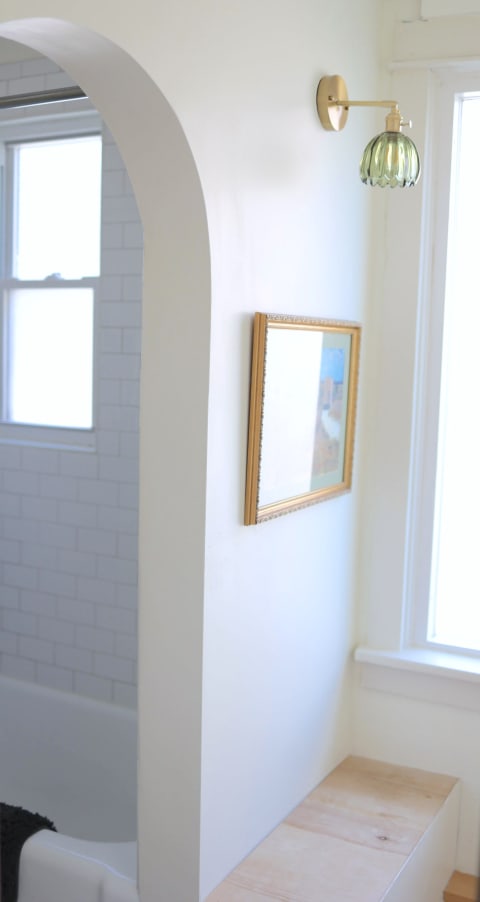 Bright bathroom nook featuring a bench, framed artwork, and a green glass sconce.